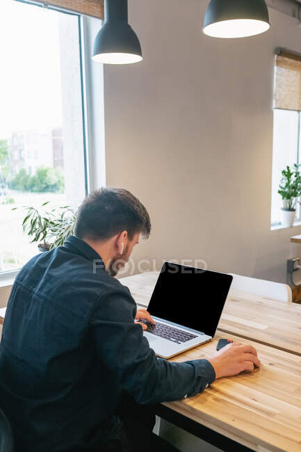 Чоловічий підприємець сидить за дерев'яним столом у творчому робочому просторі та працює над віддаленим проектом під час використання нетбука — стокове фото