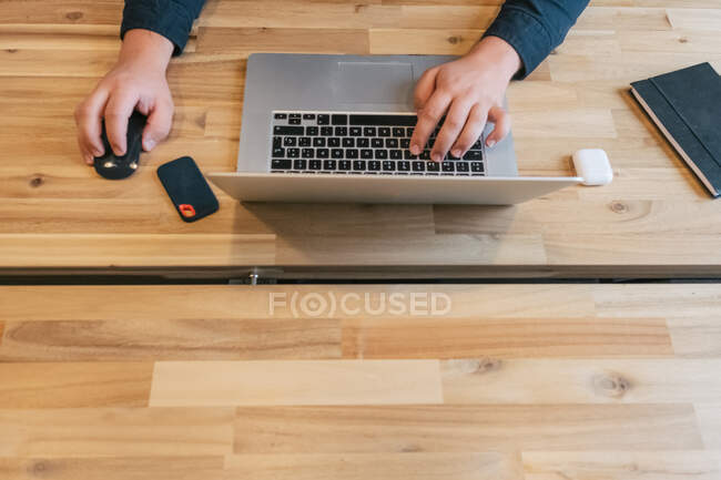 Crop male entrepreneur sitting at wooden table in creative workspace and working on remote project while using netbook — Stock Photo