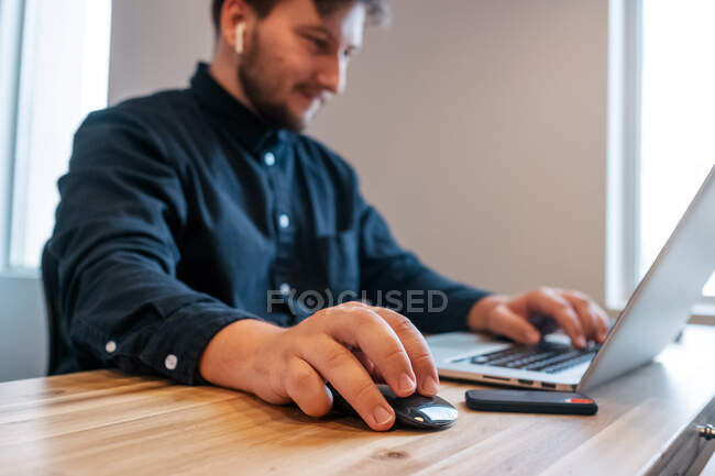 Empresário do sexo masculino sentado à mesa de madeira no espaço de trabalho criativo e trabalhando em projeto remoto ao usar netbook — Fotografia de Stock
