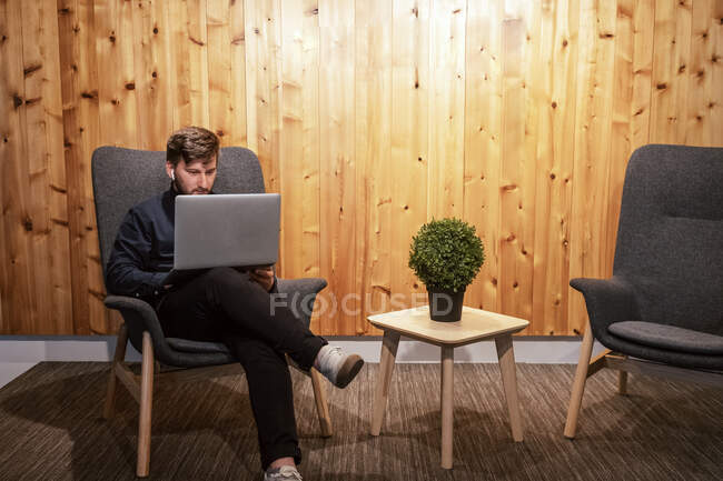 Мужній підприємець сидить за дерев'яним столом у творчому робочому місці і працює над віддаленим проектом, використовуючи нетбук. — стокове фото