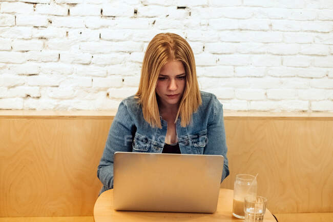 Lavoro autonomo concentrato femminile in abiti casual seduto a tavola in uno spazio di lavoro luminoso e digitando sul netbook durante il lavoro a distanza — Foto stock