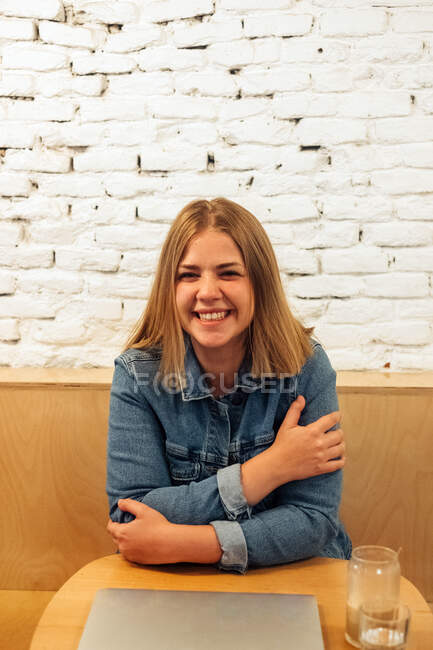 Happy female freelancer in casual shirt relaxing at table in modern workspace while having break during distant work — Stock Photo