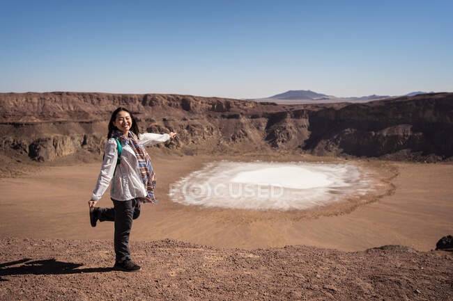 Viajante fêmea asiática feliz sorrindo com olhos fechados enquanto aponta para a superfície de cristal de fosfato de sódio dentro da cratera durante a viagem no vale do deserto com terreno rochoso — Fotografia de Stock
