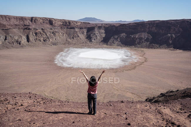Back view female traveler pointing at sodium phosphate crystal surface inside crater during trip in desert valley with rocky terrain — Stock Photo