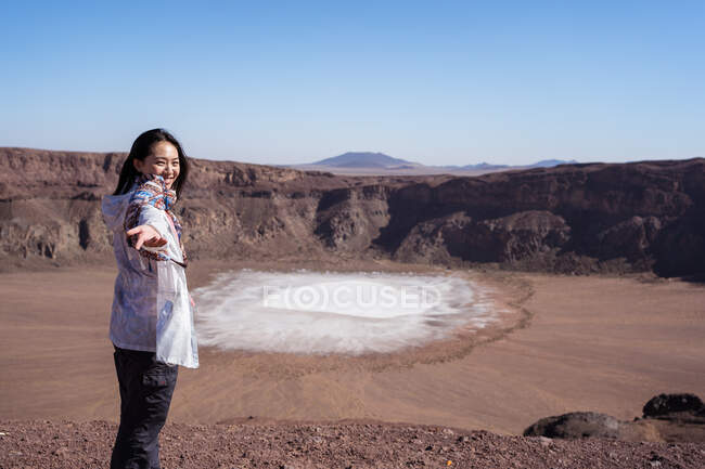 Happy Asian female traveler smiling while pointing at sodium phosphate crystal surface inside crater during trip in desert valley with rocky terrain — Stock Photo