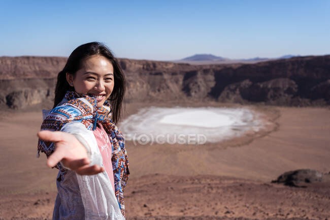Щаслива жінка - мандрівниця з Азії посміхається, коли вказує на поверхню кристалу натрію фосфату в кратері під час подорожі в пустельній долині з кам 