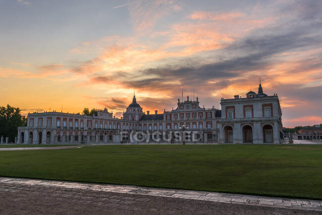 Facciata di palazzo medievale con vialetto e prati verdi sotto il cielo del tramonto — Foto stock