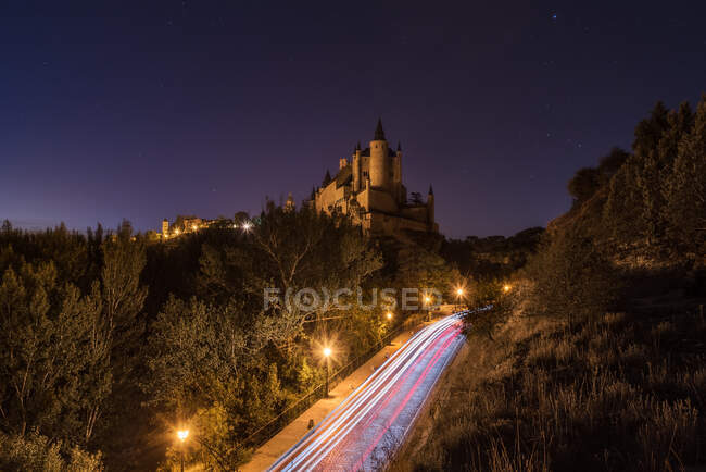 De cima da fortaleza antiga cercada por árvores e estrada luminosa contra o céu estrelado à noite — Fotografia de Stock
