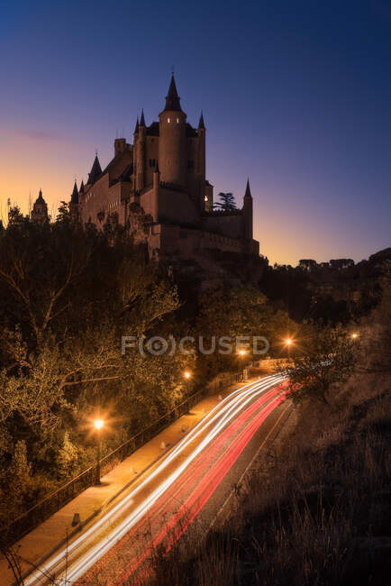 Desde lo alto de la antigua fortaleza rodeada de árboles y carretera luminosa contra el cielo estrellado por la noche - foto de stock
