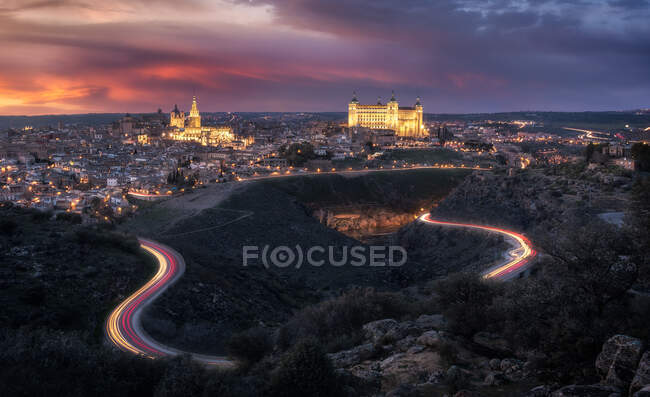 Amazing drone view of aged town with old buildings glowing during sunset and luminous highway in long exposure — Stock Photo