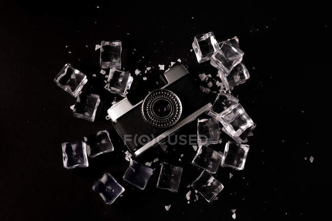 Top view of vintage photo camera surrounded by ice cubes showing concept of well preserved gadget on black background — Stock Photo