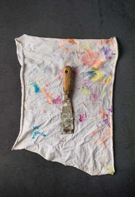 Top view of shabby scraper placed on white napkin painted in various colors — Stock Photo