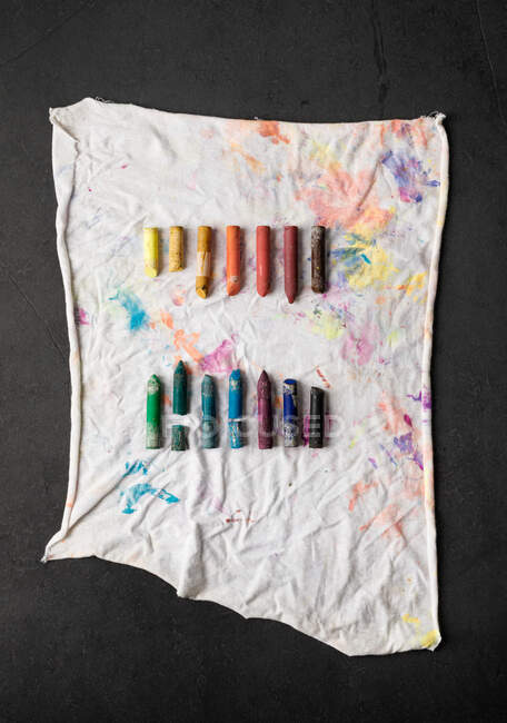 Top view of multicolored pastel colors placed in rows on piece of painted cloth — Stock Photo