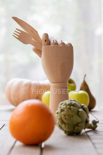 Mão de madeira criativa com garfo e faca colocados na mesa com frutas e legumes maduros — Fotografia de Stock