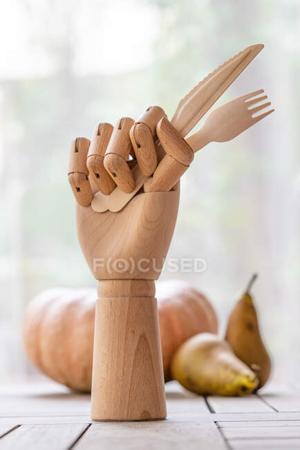 Креативная рука манекена с одноразовой вилкой и ножом, украшенным веточкой зеленой петрушки на столе в саду — стоковое фото
