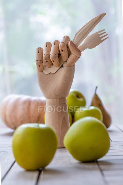 Mano de madera con cuchillo y tenedor colocados en la mesa con frutas y verduras frescas para una dieta nutritiva - foto de stock