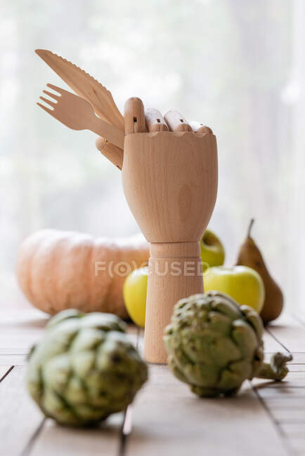 Mão de madeira com faca e garfo colocada na mesa com frutas e legumes frescos para uma dieta nutritiva — Fotografia de Stock