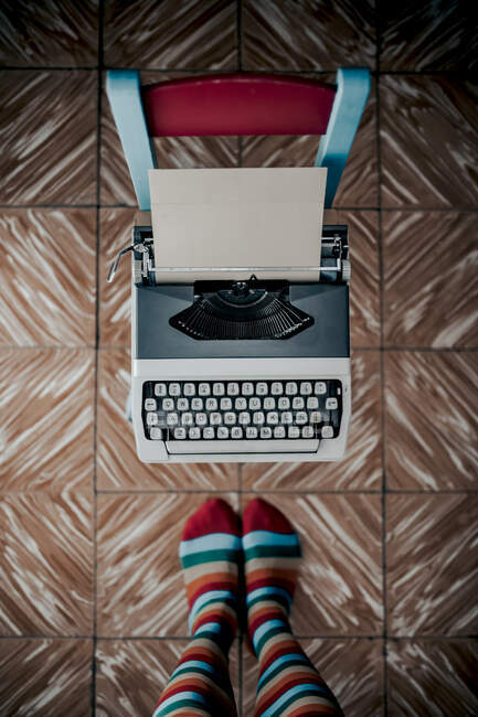 Vista superior de los pies en calcetines desnudos de pie cerca de la máquina de escribir a la antigua - foto de stock