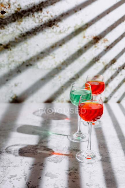 Glasses filled with colorful liquids on concrete surface in bright sunlight — Stock Photo