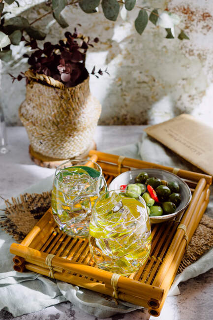 Glasses of cocktails with ice cubes with green olives on wooden tray — Stock Photo
