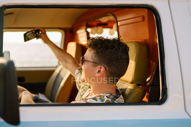 Щасливий дорослий чоловік бере селфі зі смартфоном, сидячи у фургоні — стокове фото