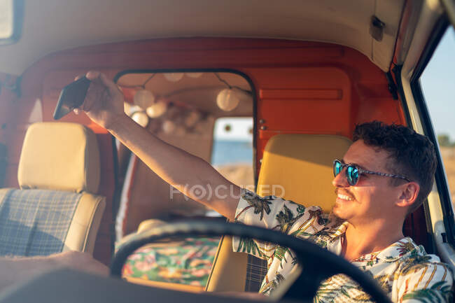 Счастливый взрослый мужчина делает селфи со смартфоном, сидя в фургоне — стоковое фото