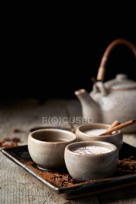 Masala chai servito in ciotole di ceramica con anice stellato e bastoncini di cannella disposti su tavolo di legno con teiera e pezzo di stoffa — Foto stock