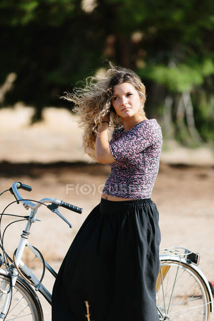 Ruhige Frau im Sommeroutfit, die an sonnigen Tagen mit dem Fahrrad im Park spazieren geht und wegschaut — Stockfoto