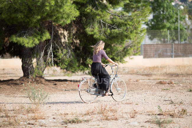 Calma femminile in abito estivo a piedi con bici in parco nella giornata di sole e guardando altrove — Foto stock