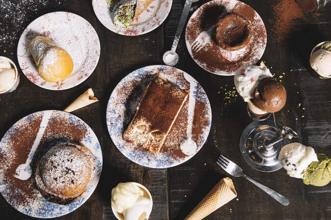 Alto ángulo de Tiramisú adornado con cacao en polvo colocado en la mesa con magdalena y pastel de chocolate espolvoreado con azúcar en polvo - foto de stock