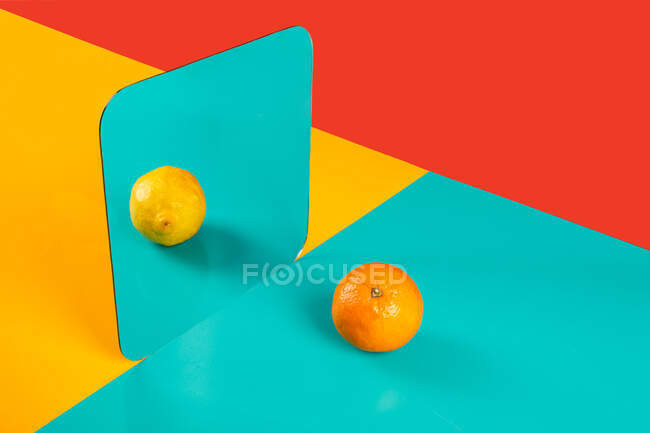 Vibrant background with mirror reflection of fresh orange as lemon on blue surface in composition with empty red and yellow areas like concept of perception in three dimensional space and distortion of imagination — Stock Photo