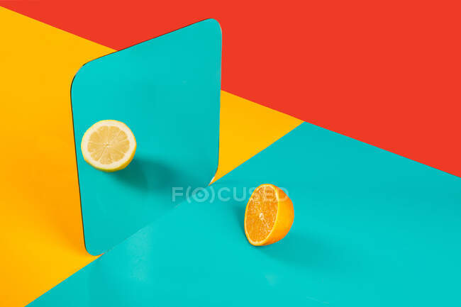 Яркий фон с зеркальным отражением половины свежего апельсина в виде лимона на голубой поверхности в композиции с пустыми красными и желтыми областями, такими как концепция восприятия в трехмерном пространстве и искажение воображения — стоковое фото