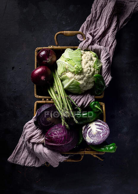 Vista dall'alto di varie verdure fresche mature con asciugamano viola in cesto di vimini posto sulla superficie scura come concetto di cibo sano — Foto stock