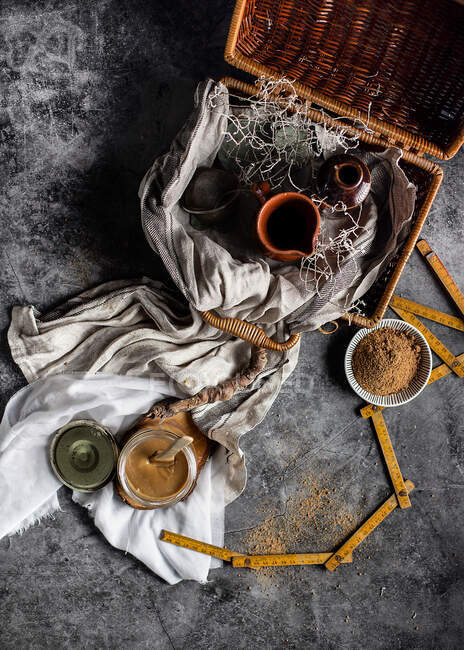 From above still life of yummy caramel with cane sugar powder as ingredient placed on table in arrangement with tea set in wicker basket and various decor elements against blurred dark background in studio — Stock Photo