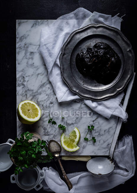 Vista superior da placa de metal com geléia de ameixa colocada sobre tecido branco na mesa, juntamente com fatias de limão e molho de salsa — Fotografia de Stock