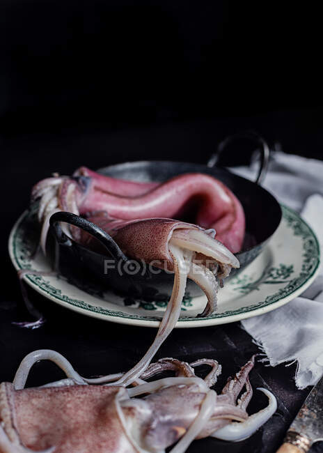 Rohes Fleisch von Tintenfischen in Metallschüssel auf dem Tisch in der Küche auf schwarzem Hintergrund — Stockfoto
