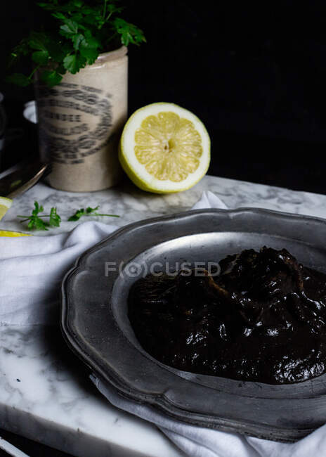 Placa de metal com geléia de ameixa colocada sobre tecido branco na mesa, juntamente com fatias de limão e molho de salsa — Fotografia de Stock