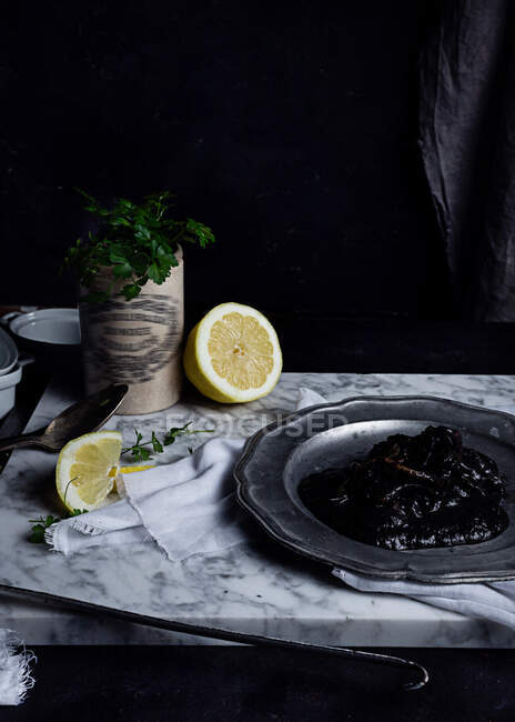 Placa de metal com geléia de ameixa colocada sobre tecido branco na mesa, juntamente com fatias de limão e molho de salsa — Fotografia de Stock