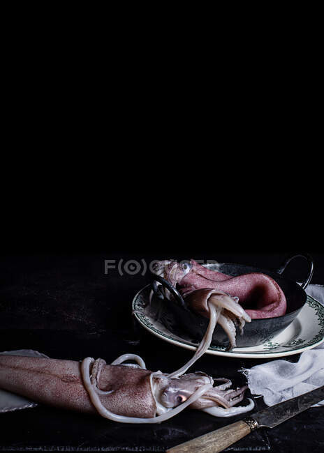 Viande non cuite de calmars placée dans un bol en métal sur la table dans la cuisine sur fond noir — Photo de stock