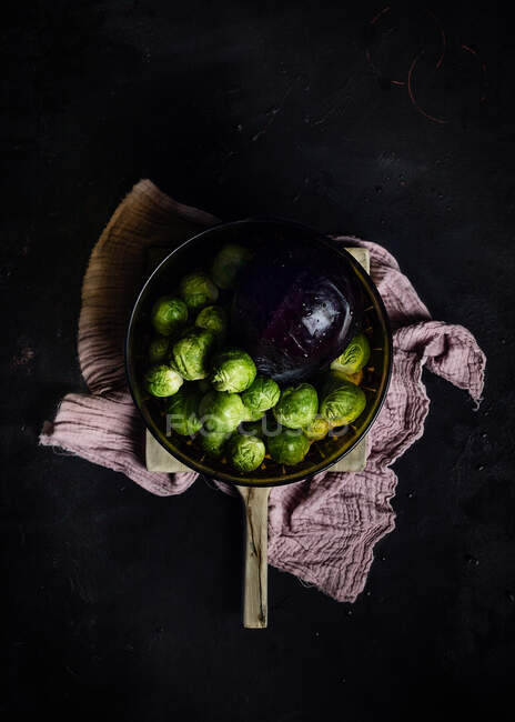Top view of ripe Brussels sprouts and purple cabbage in ceramic bowl placed on cutting board and kitchen towel — Stock Photo