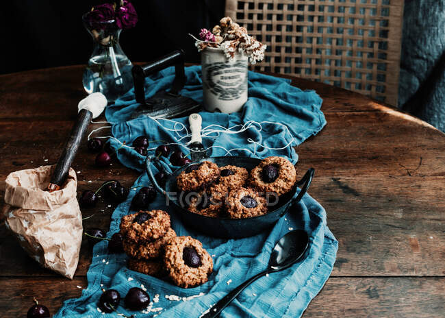 D'en haut de délicieux biscuits aux cerises cuits au four placés sur une table en bois avec un morceau de tissu et du fer vintage — Photo de stock