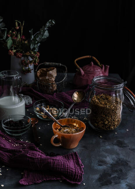 De dessus de muesli dans un bocal en verre et une tasse placés sur la table avec des noix et des baies séchées — Photo de stock
