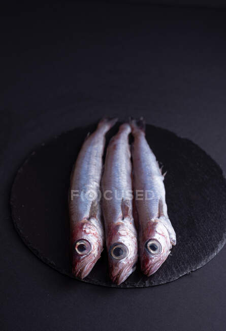 Vue du dessus du poisson cru à l'éperlan placé sur une table noire dans la cuisine — Photo de stock
