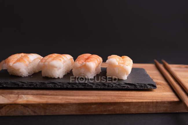 Köstliches Sushi mit Reis und Garnelen serviert auf Holzbrett mit Essstäbchen im Restaurant — Stockfoto