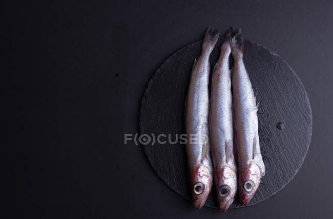 Вид зверху на сиру рибу, розміщену на чорному столі на кухні — стокове фото