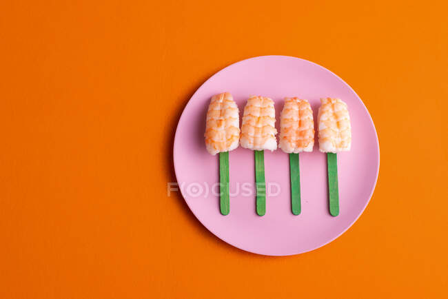 Draufsicht auf ein schmackhaftes Sushi-Set von Ebi Nigiri mit Garnelen, serviert in Form von Eis am Stiel und platziert auf einem Teller auf orangefarbenem Hintergrund im Studio — Stockfoto