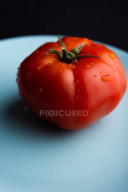 High angle closeup of ripe red tomato placed on dish in modern kitchen on black background — Stock Photo