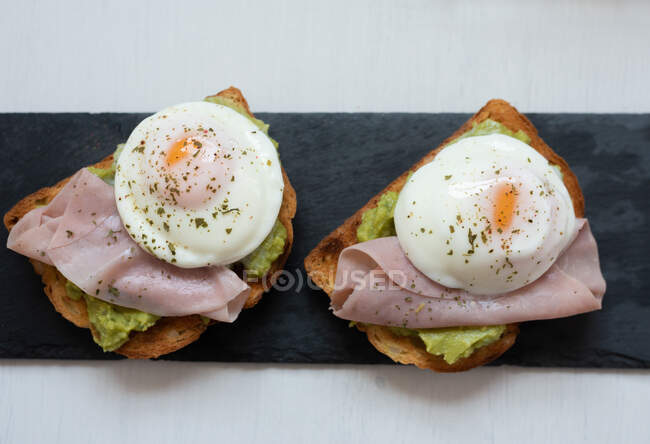 From above of appetizing toasts with guacamole garnished with tasty fried eggs and ham placed on table for breakfast — Stock Photo