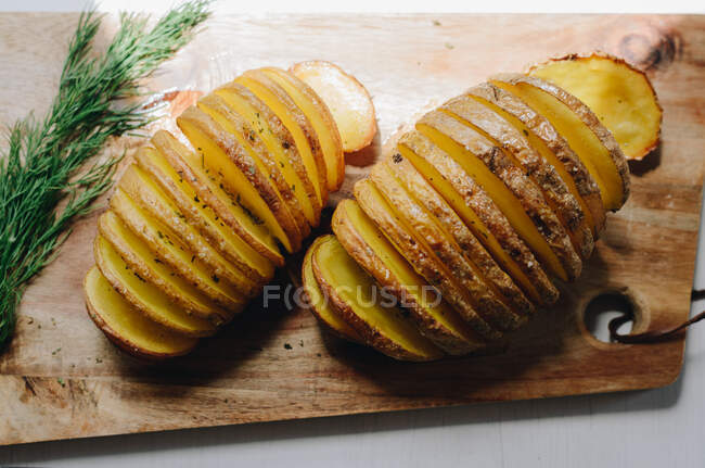 From above of tasty baked potatoes served with sprig of green dill and placed on wooden chopping board for dinner at home — Stock Photo