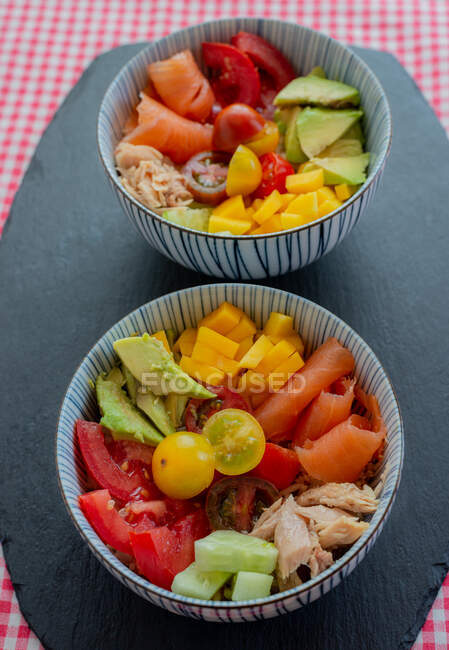 Schüsseln mit gehacktem frischem Gemüse und Fleisch von Lachs und Huhn auf den Tisch in der Küche zum Mittagessen gestellt — Stockfoto